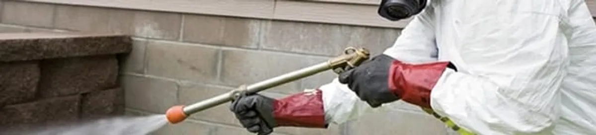 Pest control technician applying exterior insect treatment along a home foundation in Bakersfield, CA