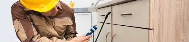 Roach exterminator applying treatment under kitchen cabinets in Bakersfield, CA
