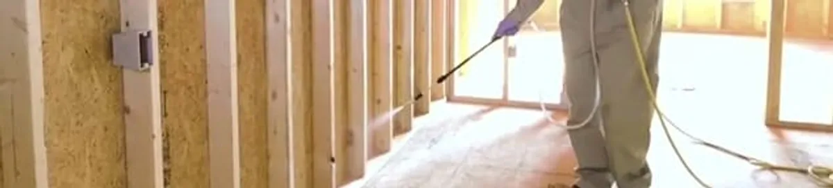Termite treatment technician applying spray along framing and unfinished walls in Bakersfield, CA