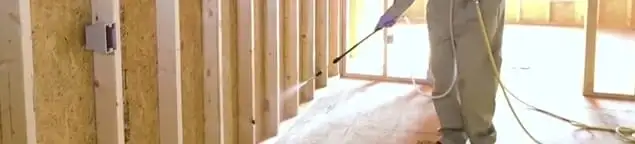 Termite treatment technician applying spray along framing and unfinished walls in Bakersfield, CA